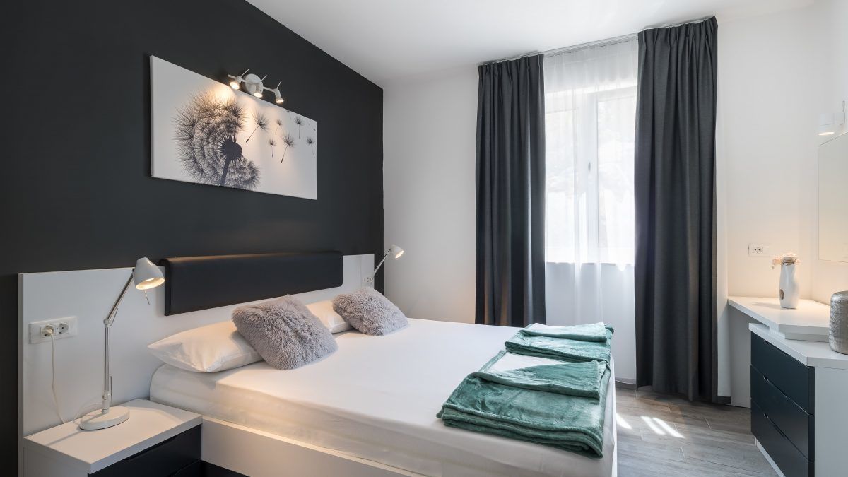 Une chambre moderne avec un grand lit, des lampes de chevet, une tête de lit, une fenêtre avec des rideaux et une petite table de chevet avec une lampe.