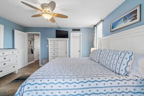 Une chambre à coucher comprenant un lit, une commode, une armoire, un ventilateur de plafond, une télévision et un tableau accroché au mur.