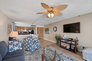A living room with a ceiling fan, a TV, a dining area, and a kitchen in the background.