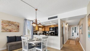 Une cuisine moderne avec des meubles blancs, un réfrigérateur noir et un coin repas comprenant une table et des chaises blanches.