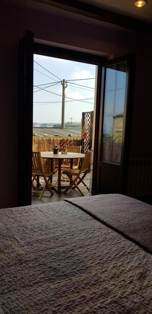 Habitació amb llit, vistes a un balcó exterior amb taula i cadires, i una finestra.