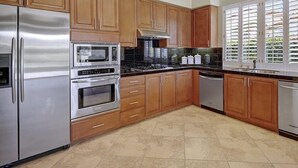 Een moderne keuken met houten kastjes, roestvrijstalen apparatuur en een groot raam met zonwering.