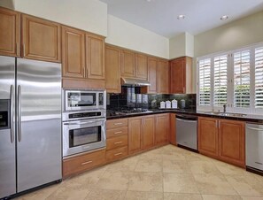 A modern kitchen with wooden cabinets, stainless steel appliances, and a large window with blinds. -  Exclusive Private Gated Country Club Home Rental - looking for yearlong renter (Palm Desert)