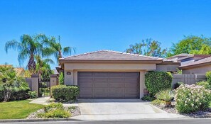 A single-story house with a garage, surrounded by well-maintained landscaping and palm trees.