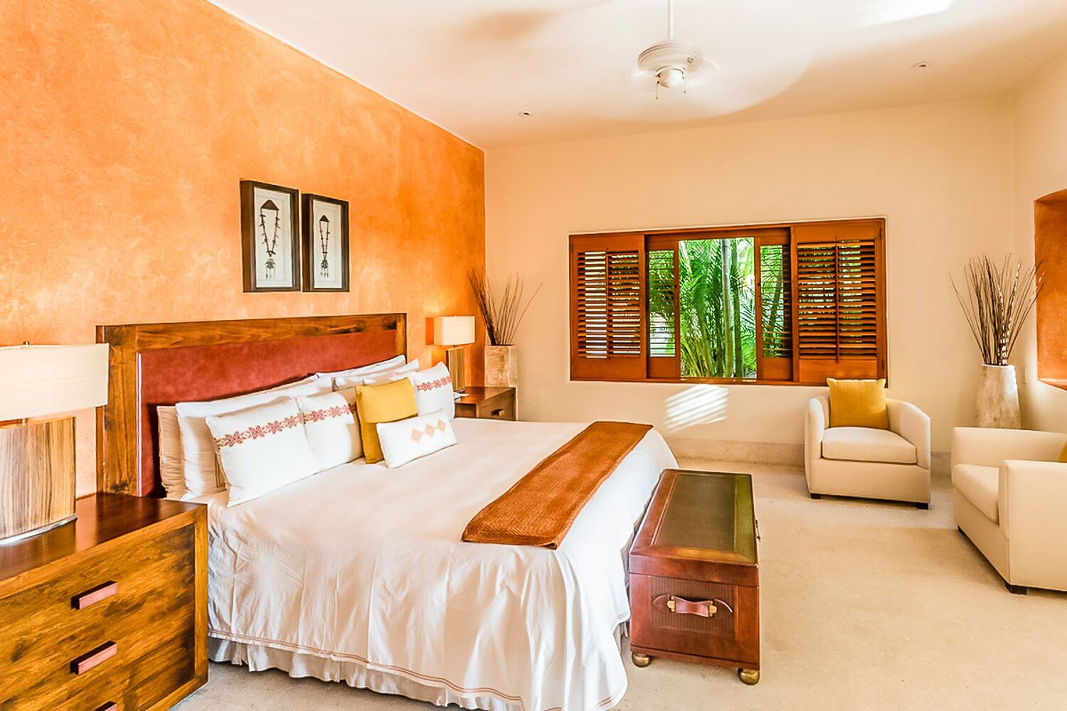 Habitación de hotel con una cama grande, cabecera de madera, una zona de estar con dos sillones, una mesita y una ventana con contraventanas de madera.
