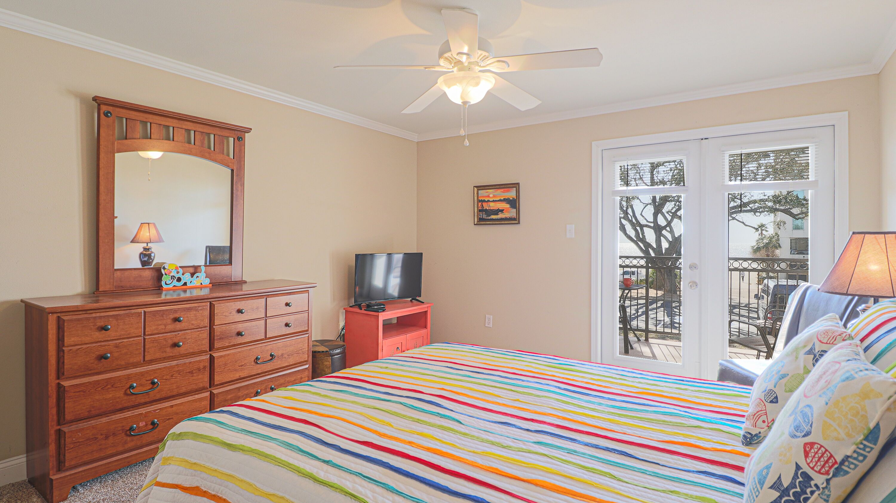 Une chambre avec un lit, une commode, une télévision, un ventilateur de plafond et un balcon avec vue.
