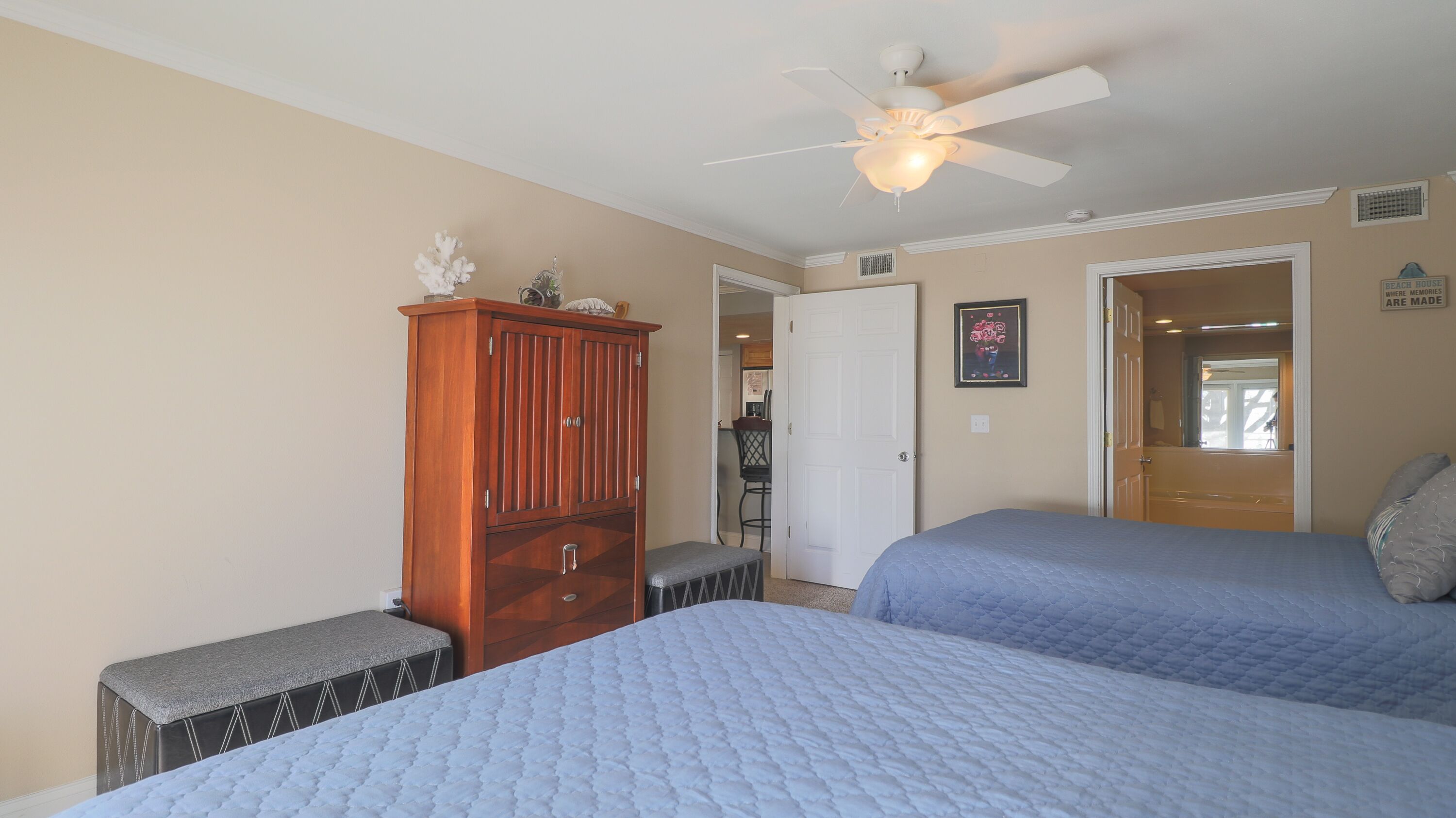 A bedroom with two beds, a wooden cabinet, a ceiling fan, and a door leading to another room.
