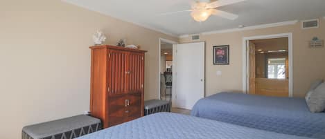 A bedroom with two beds, a wooden cabinet, a ceiling fan, and a door leading to another room.