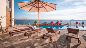 Un área junto a la piscina con sillones de descanso, una sombrilla y vista al mar.