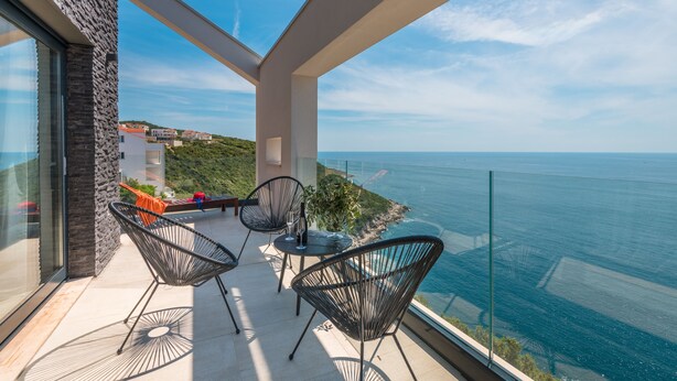 Un balcón con dos sillas y una mesa, con vista al paisaje costero.