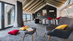 Un dormitorio moderno con techo inclinado, un ventanal grande, una cama, un sillón de lectura y una mesita.
