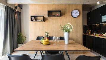 A modern dining area with a wooden table, black chairs, a clock, and a potted plant.