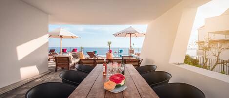 A wooden table with black chairs and a watermelon centerpiece, overlooking a beach.