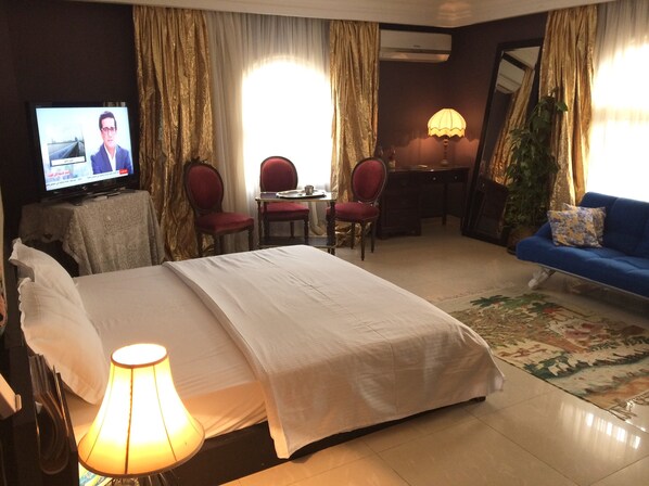 A hotel room with a bed, a desk, two chairs, a television, and a sofa. - Sunny spacious studio in New Cairo (New Cairo)
