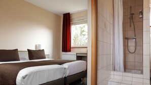 A hotel room with a bed, a desk, a shower, and a window with curtains. - Hôtel La Clef Des Champs (Biesheim)