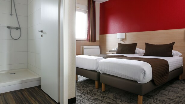 A hotel room with a shower, two beds, a red accent wall, and a window with curtains. - Hôtel La Clef Des Champs (Biesheim)