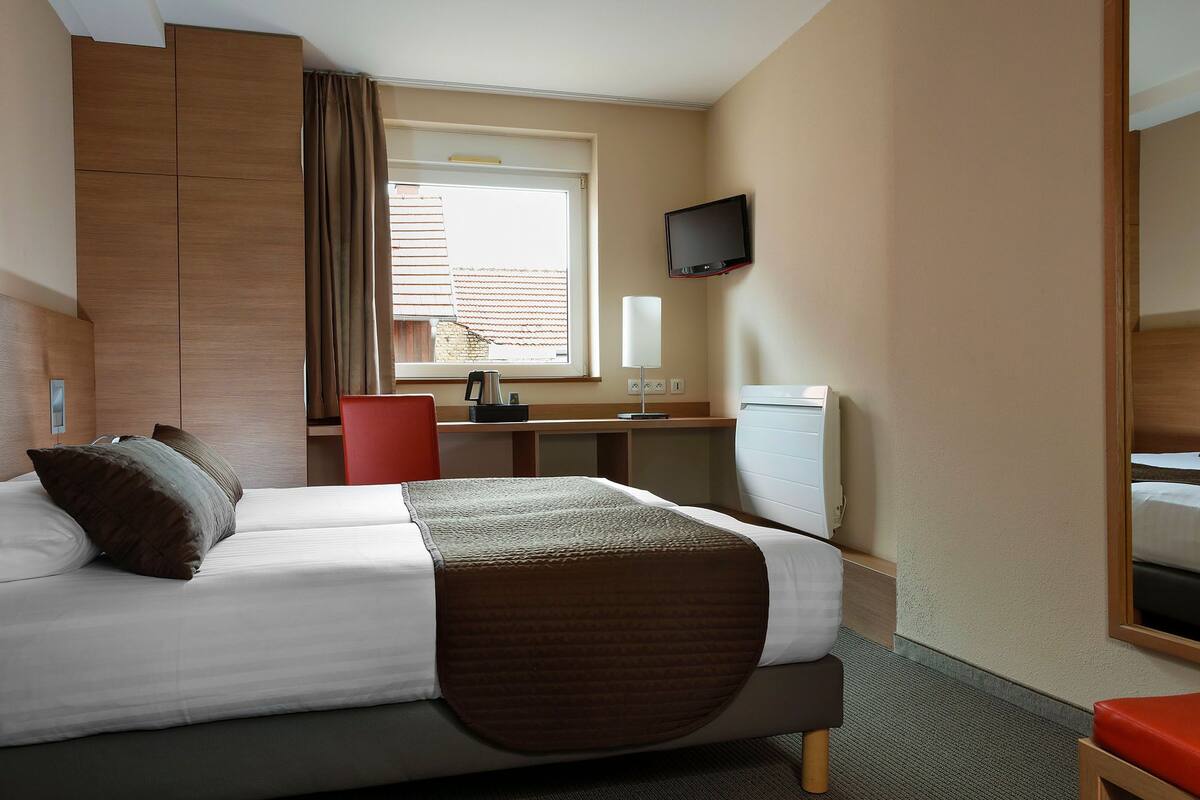 A hotel room with a bed, a desk, a chair, a TV, and a window with blinds.