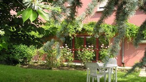 A garden with a white plastic table and chairs, surrounded by lush greenery and flowering plants. - Hôtel La Clef Des Champs (Biesheim)