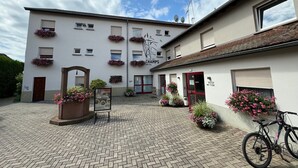 A hotel with a courtyard, flower boxes on the facade, and a bicycle parked outside. - Hôtel La Clef Des Champs (Biesheim)