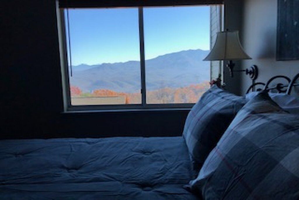A bedroom with a large window, a bed with blue bedding, and a wall-mounted lamp.