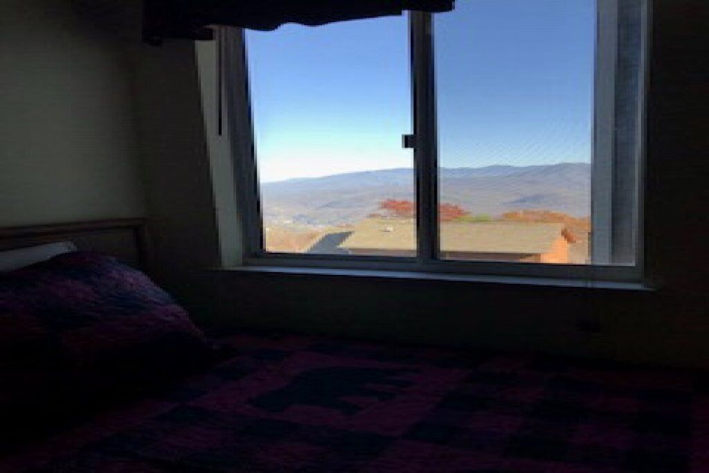 Una stanza con un letto e un'ampia finestra che offre vista su un paesaggio con montagne e cielo sereno.