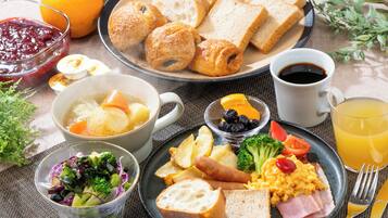 Una mesa de desayuno con pan, bollería, huevos, salchichas y ensalada.