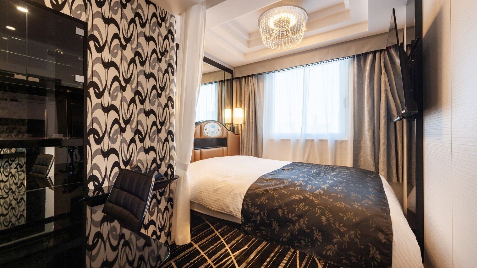 Een hotelkamer met een bed, een bureau, een stoel, een kroonluchter en gordijnen.