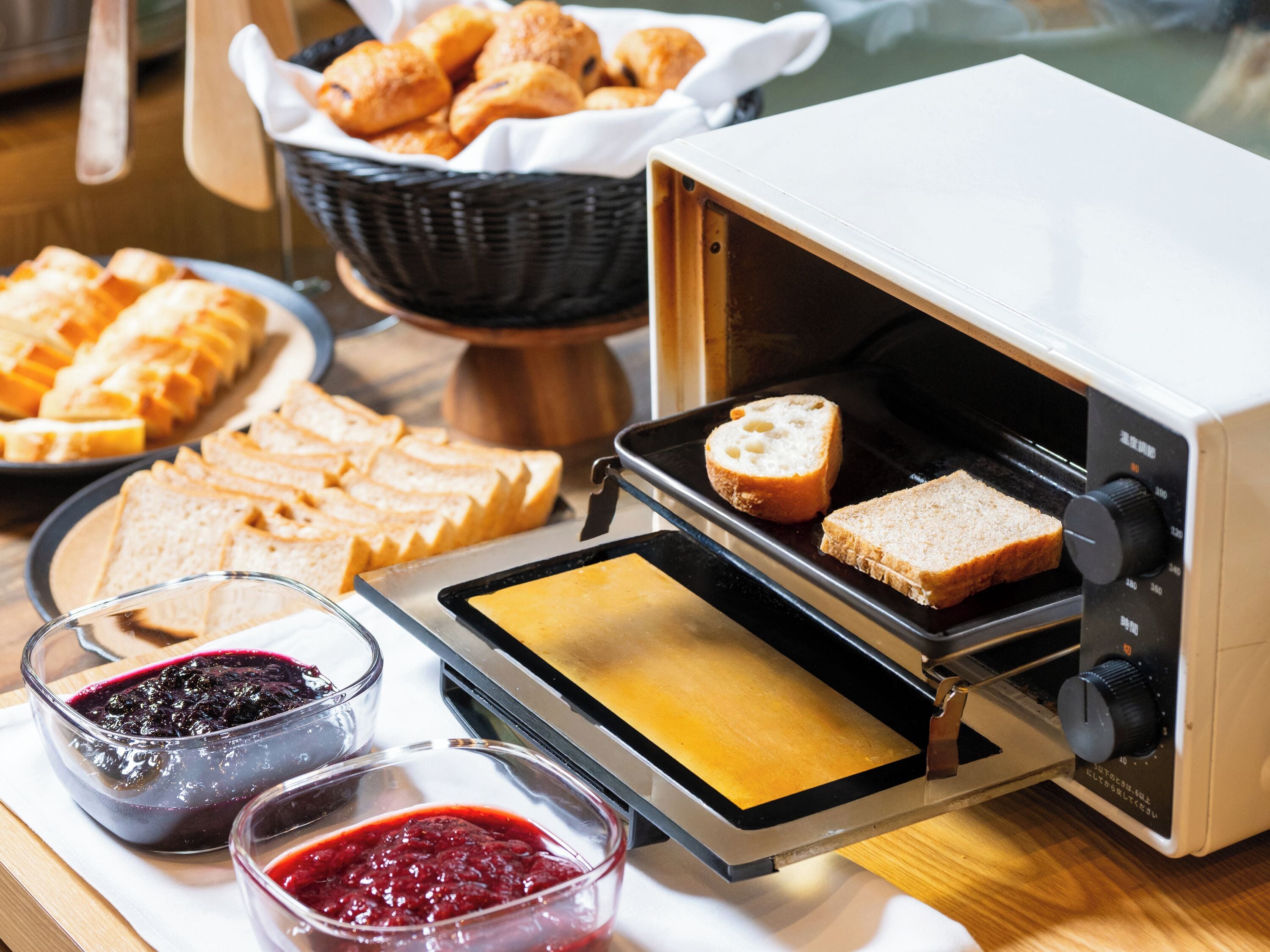 A toaster oven with bread and pastries on a table.