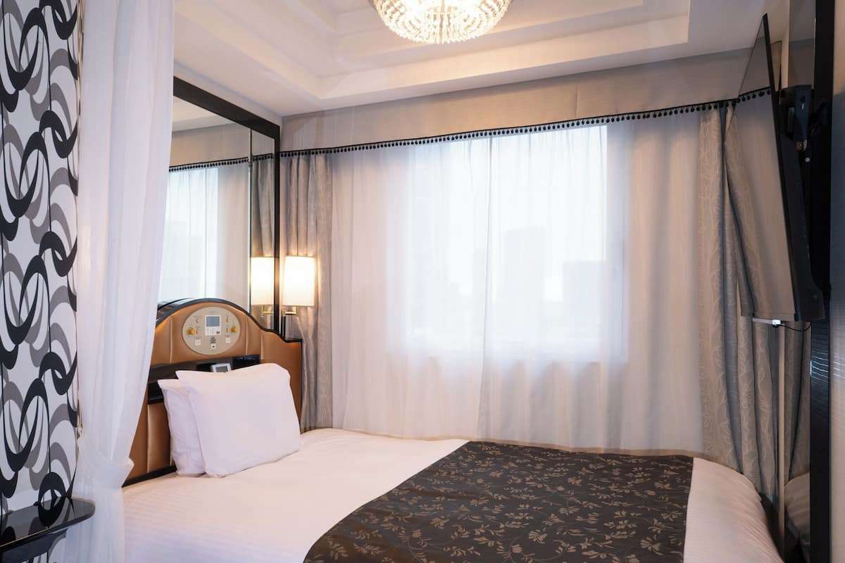 A hotel room with a large bed, a bedside table, a mirror, and a chandelier.