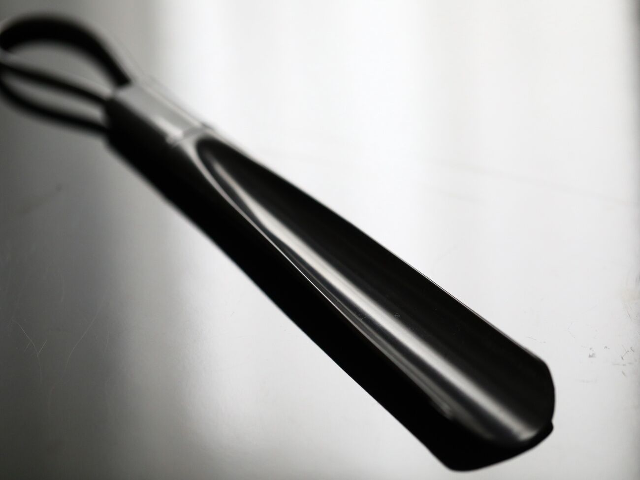 A black object with a handle, possibly a tool or utensil, against a plain background.