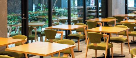 Un comedor interior moderno con mesas de madera y sillas tapizadas de verde, amplias ventanas que ofrecen vistas a la vegetación.