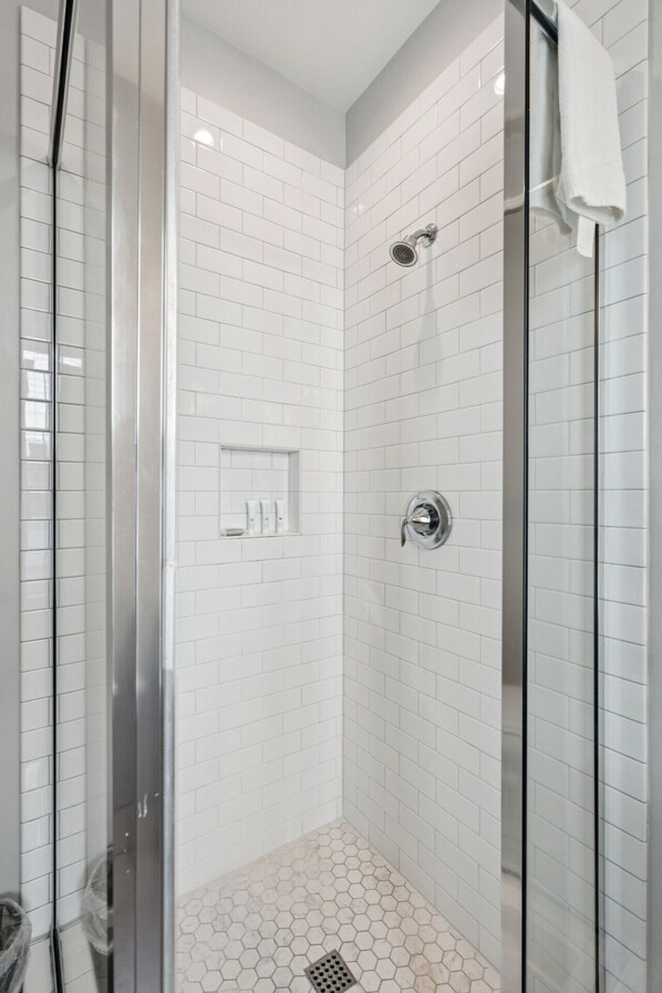 A modern shower with white tiles, a glass door, and a white towel hanging on the wall.