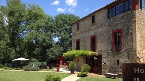 A stone building with red window frames, a paved pathway, and a well-maintained lawn. - Hotel Masia la Palma (Cabanelles)