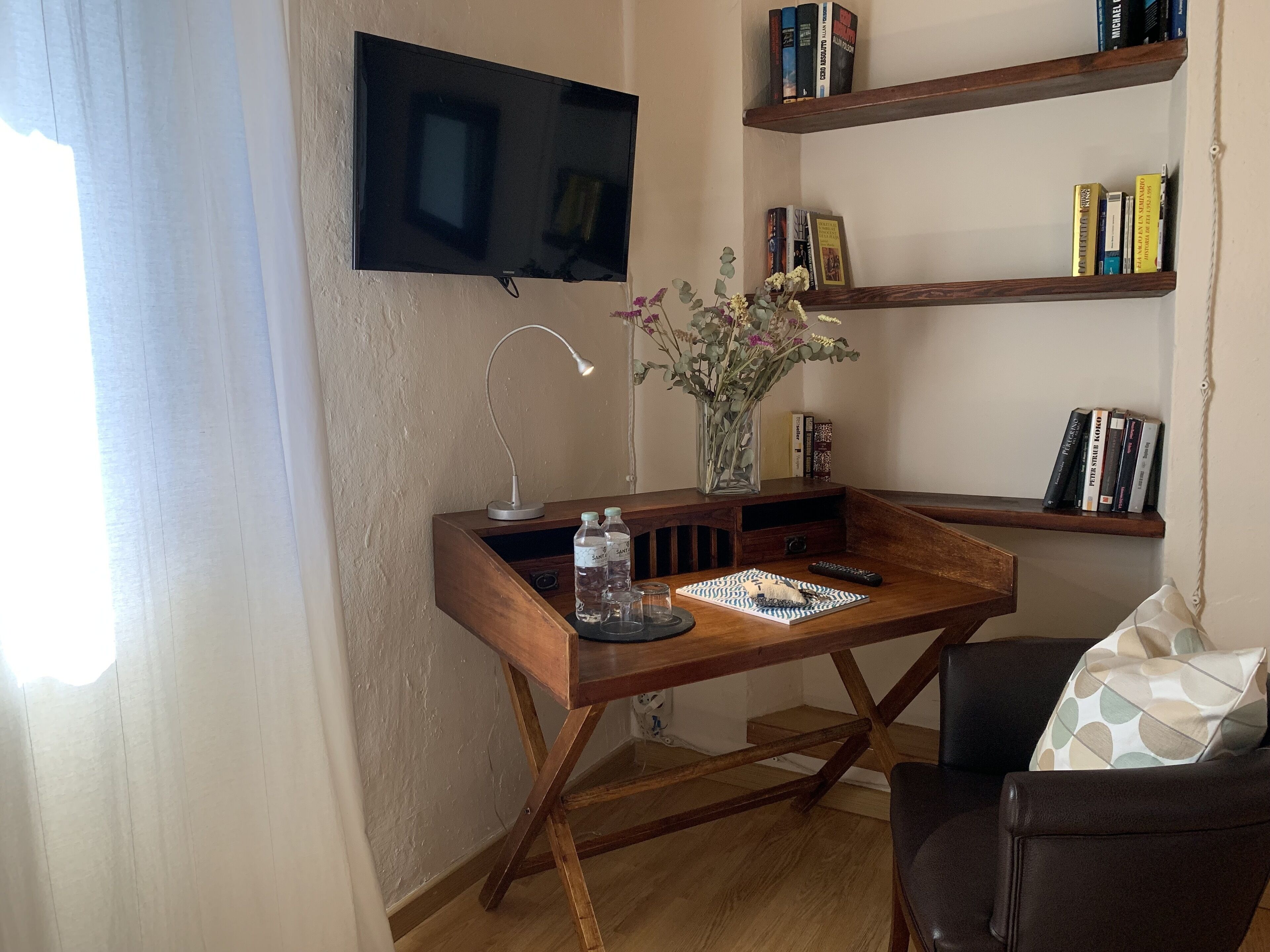 A cozy living room with a wooden desk, a flat-screen TV, a bookshelf, and a comfortable chair.