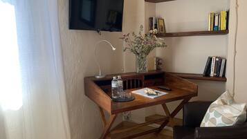 A cozy living room with a wooden desk, a flat-screen TV, a bookshelf, and a comfortable chair.