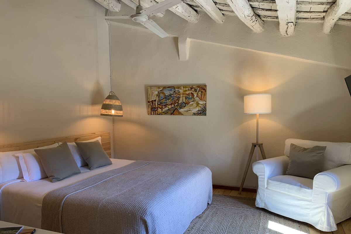 Ein Schlafzimmer mit Bett, Nachttisch, Lampe und einem Sessel.