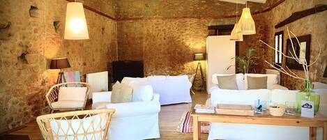 Un salon chaleureux avec un mur en pierre, des meubles blancs, une table basse en bois et des luminaires suspendus.