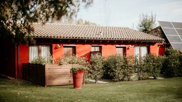 A red building with a tiled roof, wooden shutters, and a garden with a large planter and shrubs.