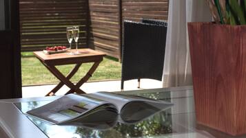 Een glazen tafel met een tijdschrift, een houten bijzettafeltje met een glas wijn en aardbeien, en een potplant.