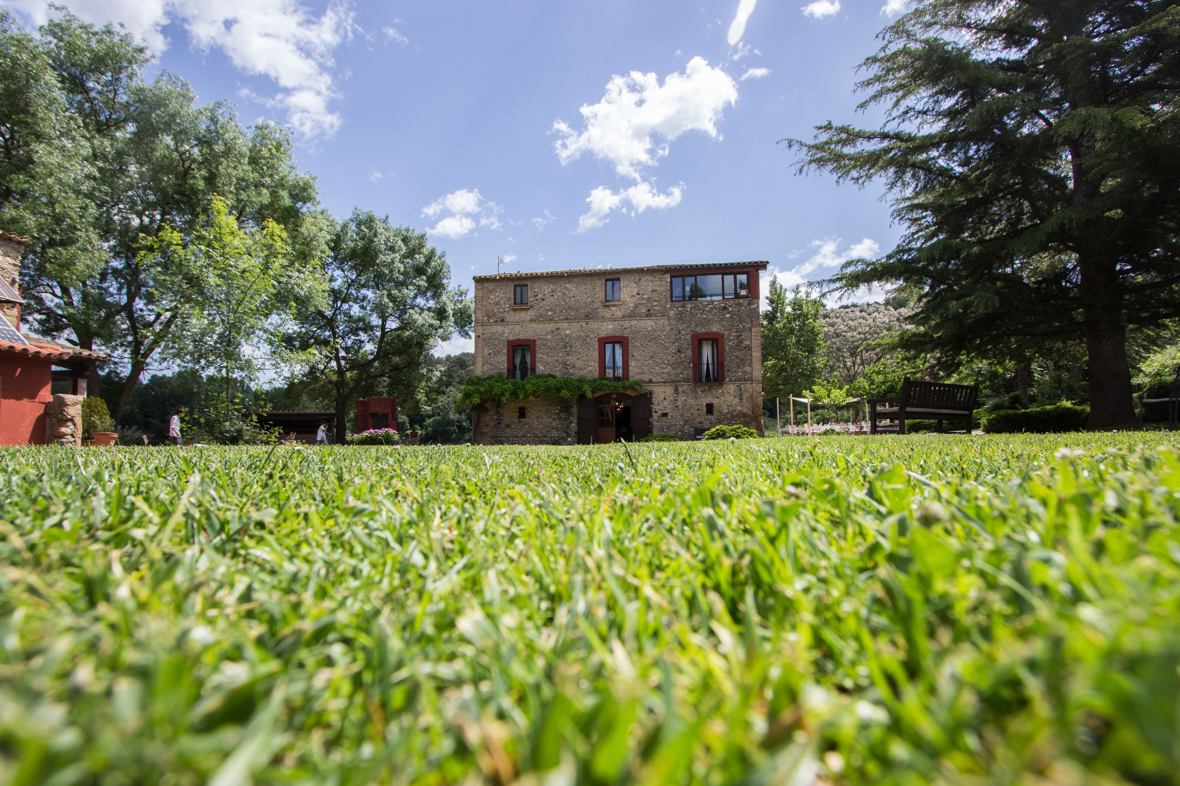 A stone building with a red roof, surrounded by lush green grass and trees.