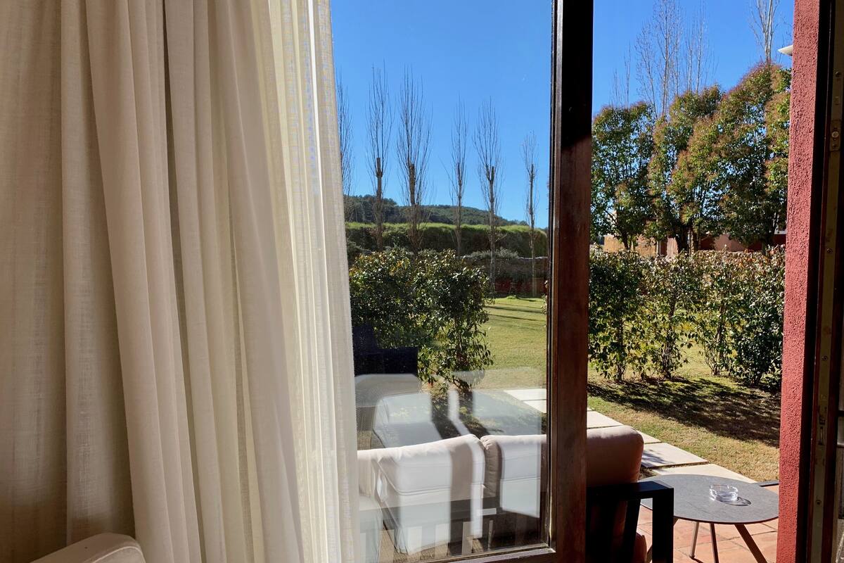 Ein Zimmer mit Gartenblick, ein Fenster mit Vorhängen, ein Sofa und ein kleiner Tisch.