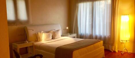 A bedroom with a bed, bedside tables, a chair, a lamp, and a window with curtains.