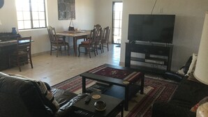 A living room with a sofa, a coffee table, a TV, a dining table with chairs, and a patterned rug. - Tranquil Retreat with Gorgeous near 360-degree Mountain Views! (Rio Rico)