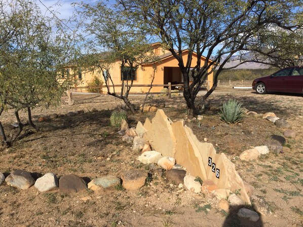 A desert landscape with a building, rocks, and sparse vegetation. - Tranquil Retreat with Gorgeous near 360-degree Mountain Views! (Rio Rico)