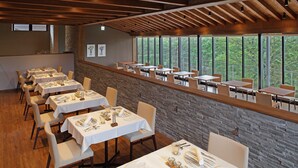 A restaurant with multiple tables and chairs, a stone wall, and large windows offering a view of trees. - Regina Resort Karuizawa Mikageyousui (Karuizawa)