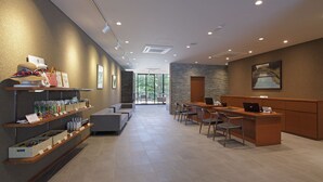 A modern hotel lobby with a reception desk, seating area, and shelves with amenities. - Regina Resort Karuizawa Mikageyousui (Karuizawa)