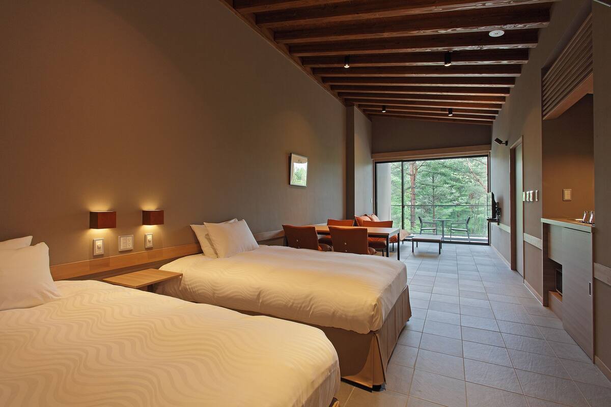 Quarto de hotel com duas camas, área de refeições e vista para o exterior.