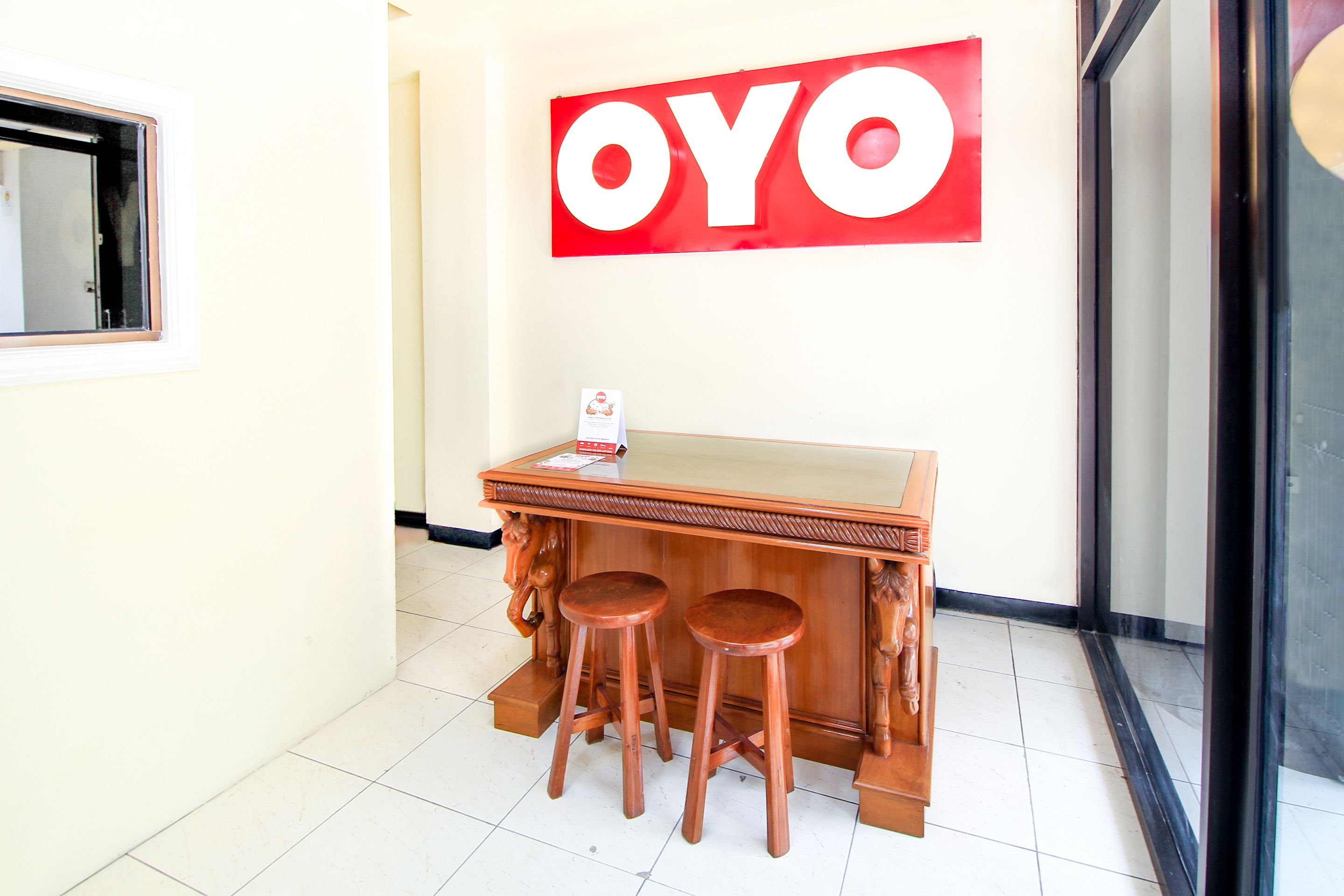 A reception area with a wooden counter, two stools, and a 'OYO' sign on the wall.