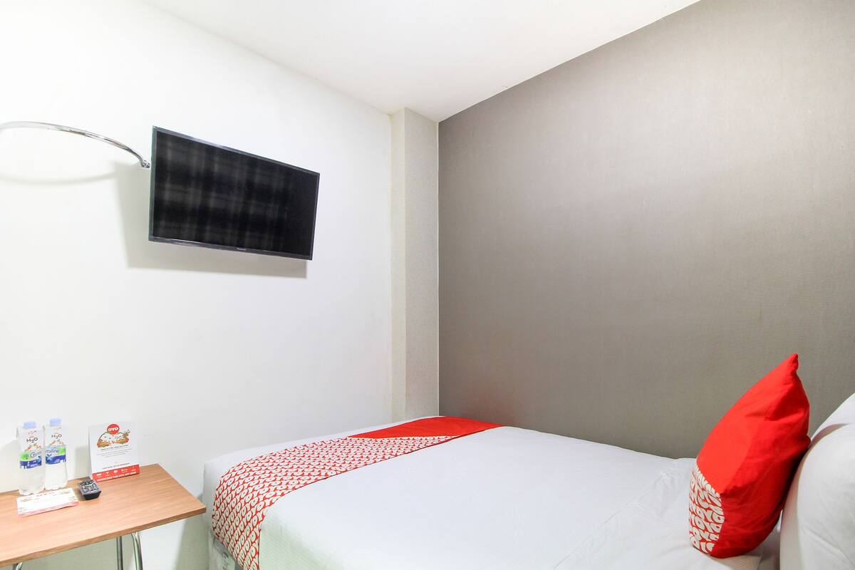 Ein Hotelzimmer mit einem Bett, einem Nachttisch mit Fernbedienung und einem flachbildfernseher an der Wand.