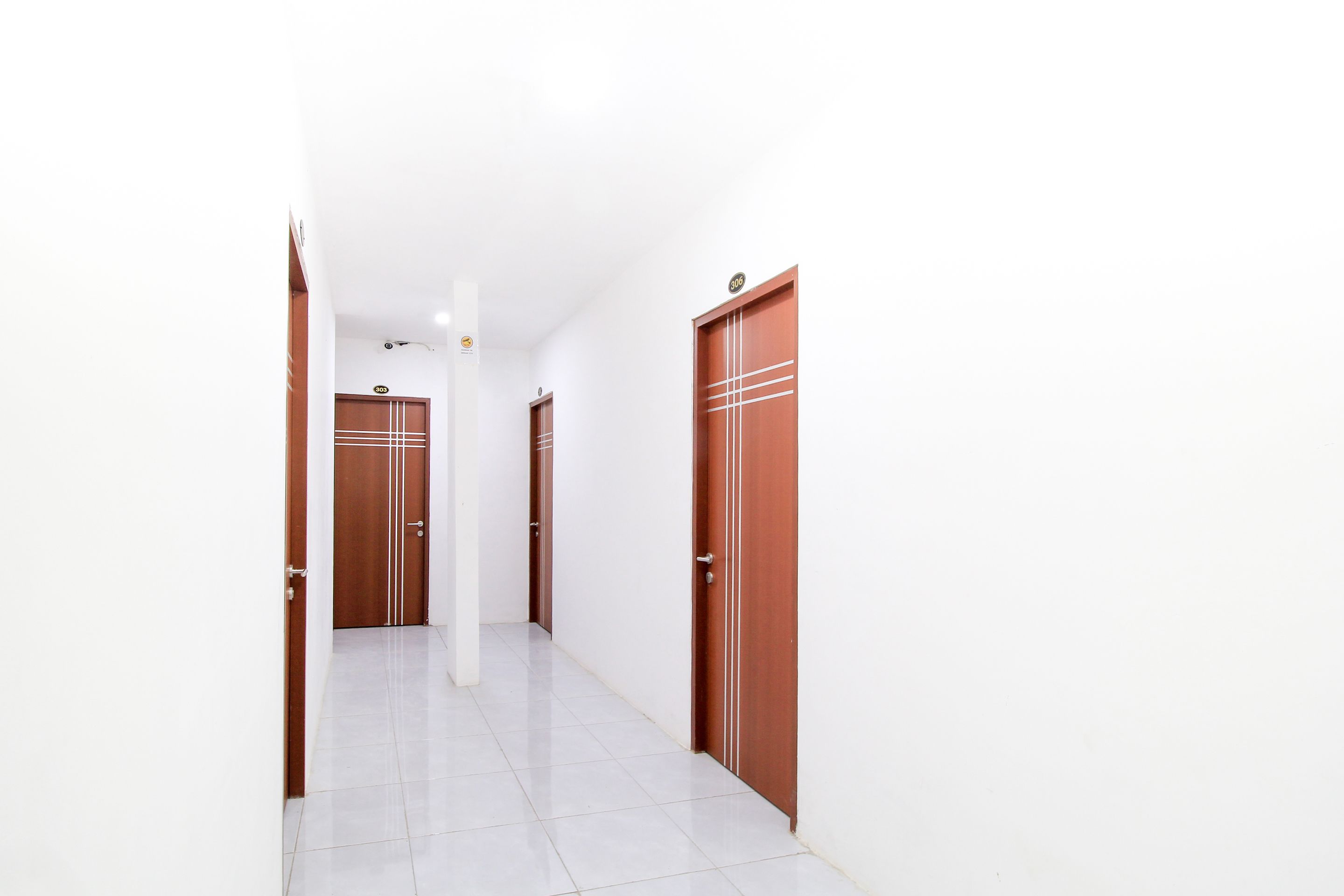 A corridor with white tiled flooring and wooden doors with metal handles.